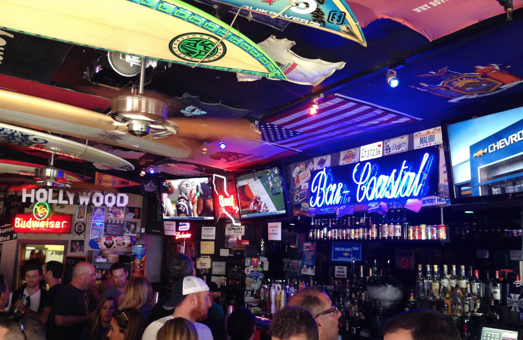 Image shows a crowd gathered at Bar Coastal, drinking and watching sports games on the tv. Bar-Coastal is one of the best bars in NYC to watch the Baltimore Ravens