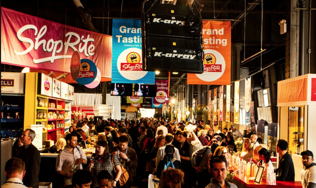 Image shows masses gathered at the NYC Wine and Food Festival, interacting with different vendors. 