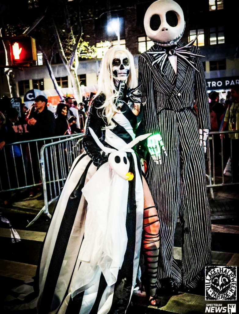 Image shows a couple dressed as Jack and Sally from The Nightmare Before Christmas, participating in the Village Halloween Parade. 
